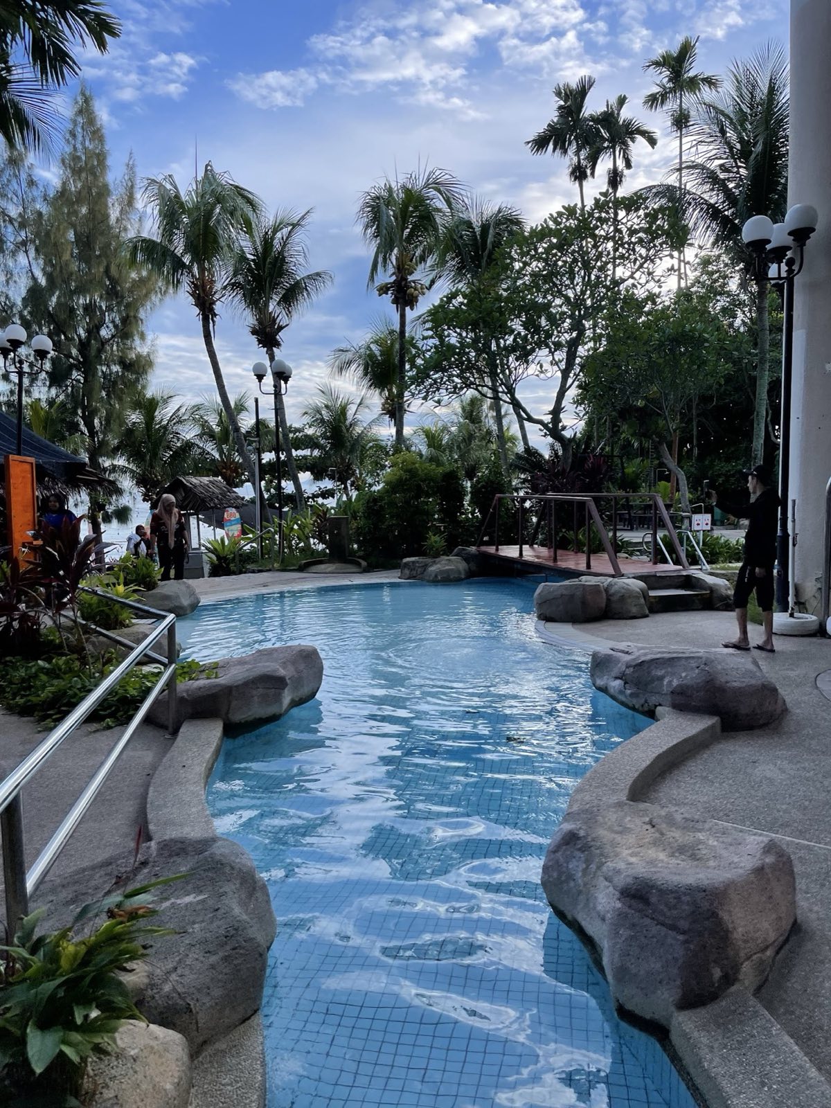 The rock-edged lagoon swimming pool at Rainbow Paradise, fringed by palm trees with the sea behind